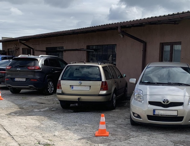 A1 Max Parkovisko - Štyri autá stoja pred budovou. Parkovisko je vyznačené stĺpikmi. Povrch je betónový.