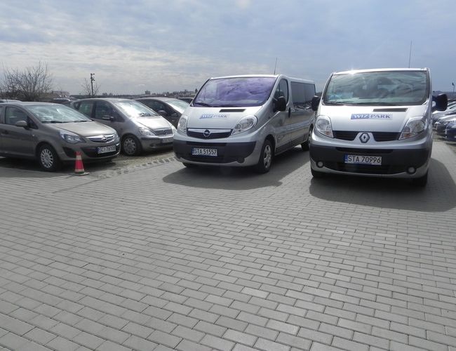 WIZ-PARK - Varios coches están estacionados en el área pavimentada. Al fondo se puede ver un cielo nublado y una fila de vehículos.