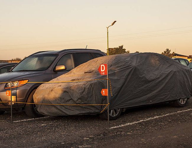 PERI Parking - El coche está bajo una cubierta gris. Está rodeado por una cuerda de protección. Junto a él están otros coches estacionados.