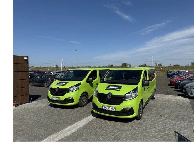 Parking Prime - Dwa zielone furgony stoją na brukowanej nawierzchni. W tle widać parkowane samochody.