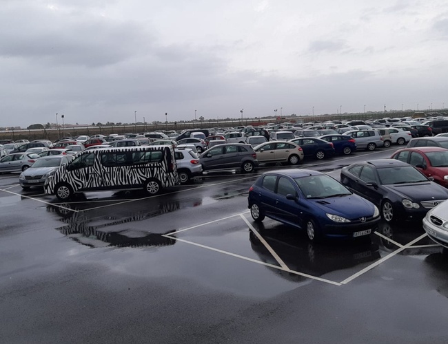 Victoria Parking Walencja - Deszczowy dzień na parkingu z zaparkowanymi autami. Widoczny pojazd z zebrą na boku. Teren jest ogrodzony.