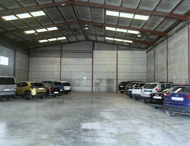Premium Parking VLC - Wnętrze dużej, zadaszonej hali z betonową podłogą. Samochody są zaparkowane po obu stronach. Metalowy dach ma świetliki.