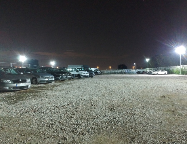 Aparcamiento del Aeropuerto 500 - Los coches están aparcados en el terreno de grava. El área está bien iluminada por farolas.