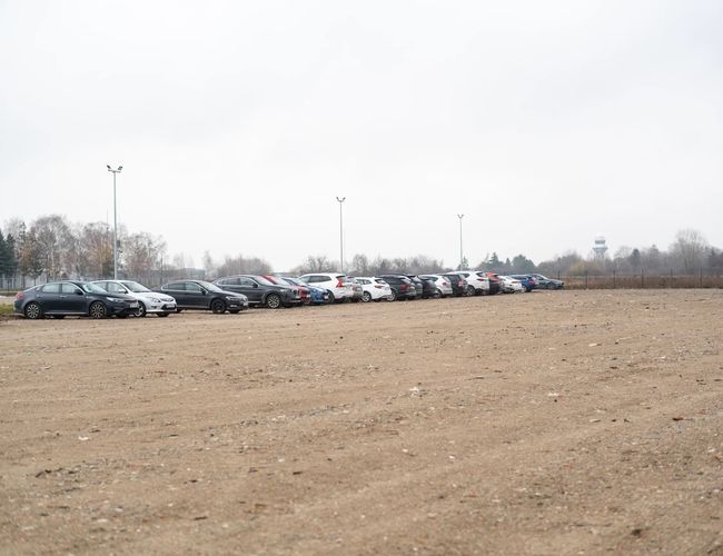 Easy Parking Standard - Na zdjęciu jest nieutwardzony parking. Kilkanaście samochodów stoi w rzędzie. Teren jest ogrodzony siatką.