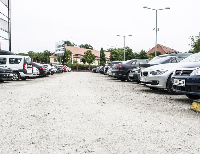 Parking Rondo - Powierzchnia żwirowa, zapełniona samochodami. Latarnie uliczne zapewniają oświetlenie.teren otoczony budynkami i zielenią.