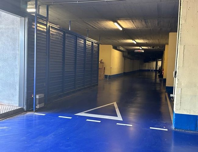 Parcare Auto și Zbor Garaj Valet - Intrare în garaj acoperit. Pardoseală albastră și linii de ghidare. Teren iluminat cu lămpi de tavan.