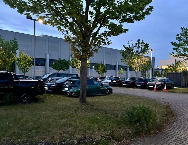 Služba parkovacieho valeta FRAir – autá stoja pri stromoch. Priestor je osvetlený mestskými lampami. Budova v pozadí je veľká.