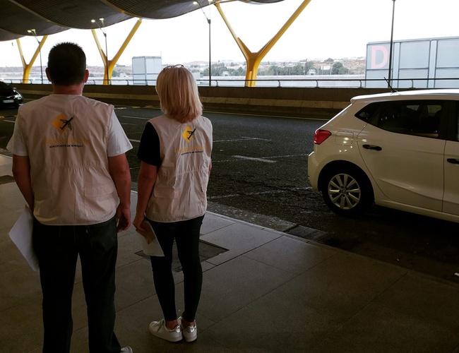 Parkovisko Pleyades Valet - Dvaja zamestnanci v reflexných vestách na parkovisku. Vedľa stojí biele auto. Na pozadí je vidieť cestu a oblohu.