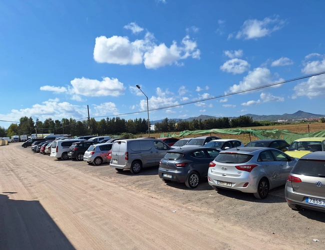 Parkovanie Low Valet – Na parkovisku je veľa zaparkovaných áut. Areál je oplotený a bez zastrešenia. Počasie je slnečné, sú viditeľné oblaky.