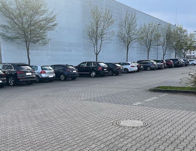 Parkering Mein-Flughafenparkplatz-Frankfurt P2 – Det står en rekke med biler på parkeringen. Til venstre kan man se trær. Plassen er tom og opparbeidet med brostein.