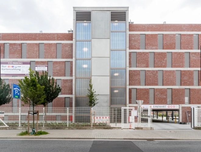 Parken Best Valet Park Service - Modernes Gebäude aus Ziegeln und Beton. Zaun, Bäume, Markierung des Parkplatzeingangs.