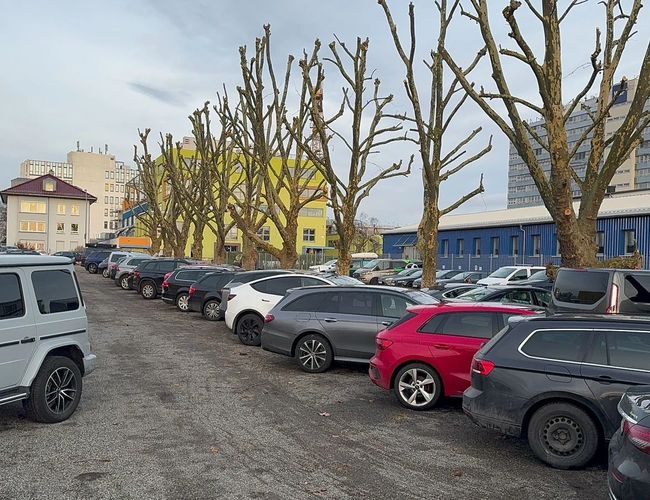 Parking Park & Go Valet – plac z kamienistym podłożem. Ogrodzony płotem, widoczne zaparkowane samochody. Dookoła budynki i drzewa.