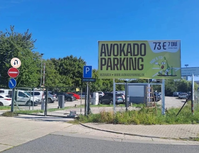 Widok parkingu „Avokado Parking” z góry, z kilkoma zaparkowanymi samochodami oraz tablicą informacyjną przy wjeździe.