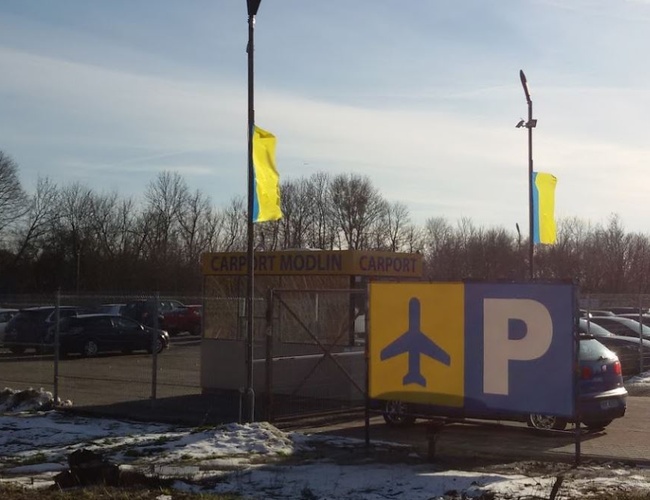 Parkovací prístrešok – Pozemok je ohradený sieťou. Viditeľné autá a tabuľky s označením parkoviska.