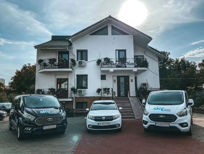 Parking Sky Park przy lotnisku w Iași – widok na teren parkingu przed budynkiem oraz samochody osobowe i bus transferowy Sky Park zaparkowane na posesji.