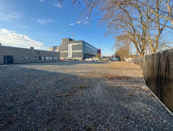 Parken ParkPoint24 Valet – Der Platz ist kieselig und offen. Auf der rechten Seite steht ein Netz. In der Ferne sind Gebäude und Bäume.