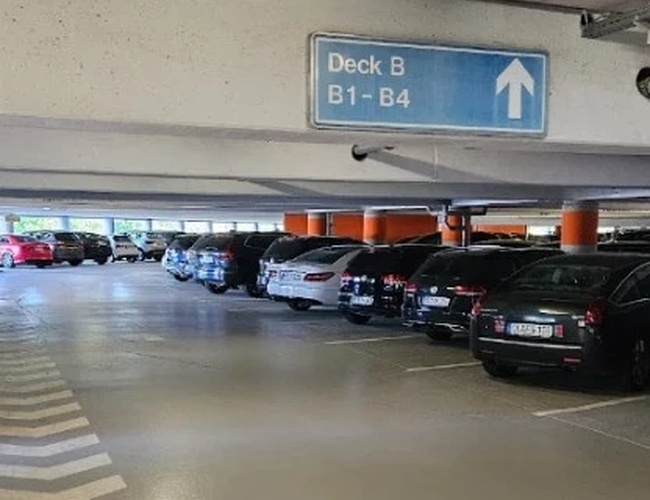 Wnętrze parkingu wielopoziomowego z szerokimi alejkami, oznakowaniem poziomów oraz rzędami zaparkowanych samochodów ułatwiającymi orientację.