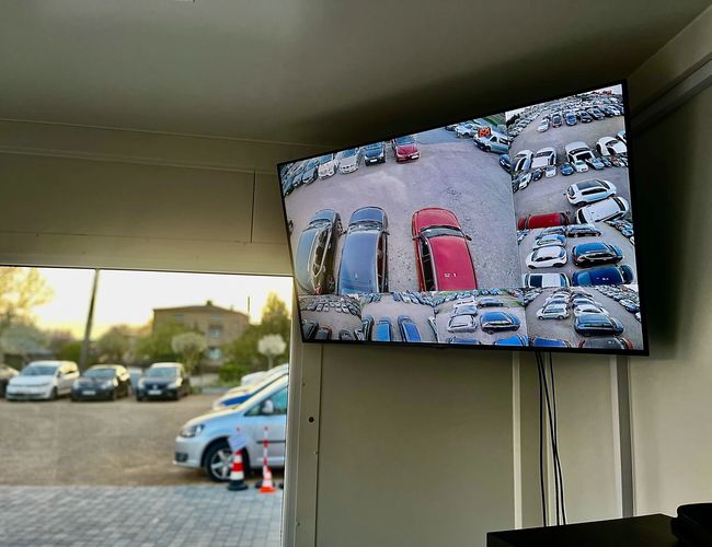 GoPark - Ekran pokazuje wiele ujęć zaparkowanych samochodów. Monitor znajduje się wewnątrz budynku.