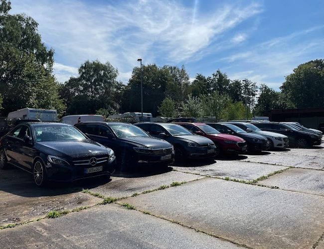 Parking Park In Fly Out - Samochody stoją równo zaparkowane. Otoczenie jest zielone, zadbane i skąpane w słońcu.