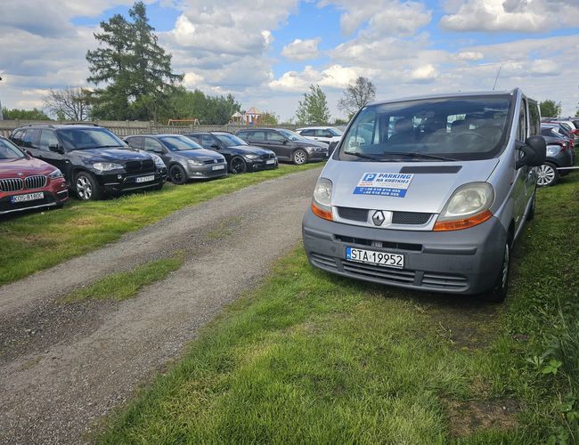 Aparcamiento en Krótkiej – Los coches están estacionados a lo largo del camino de grava. El terreno es cubierto de hierba. El entorno está cercado con árboles de fondo.