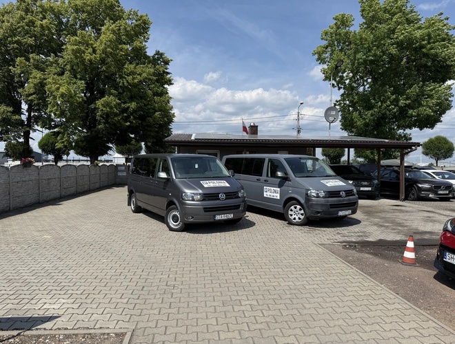 Parking Polonia – En la plaza hay varios coches. Al fondo se ve un edificio. Alrededor crecen altos árboles.
