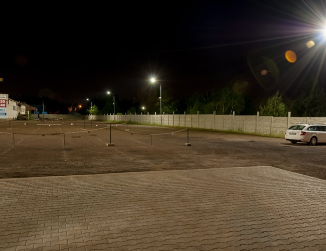 AAP-66 – Parking jest ogrodzony i dobrze oświetlony. Na placu stoją samochody. Teren jest wykonany z kostki brukowej.