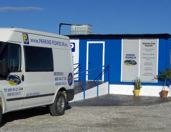 Parking PedroCar – Dostępny jest biały bus i niebieski budynek. Parking znajduje się na otwartym terenie, z widocznym ogrodzeniem.
