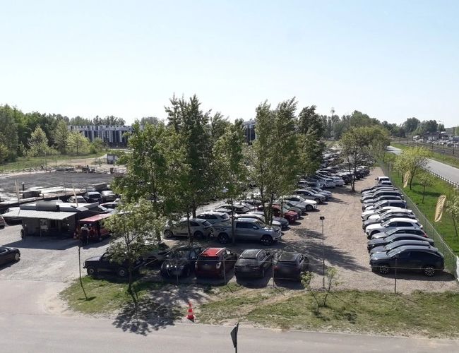 VIP Parking - przy trasie S2. Parking pełen samochodów, z nielicznymi drzewami. Teren parkingu jest przestronny i ogrodzony.