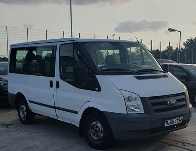 Parking Weltparking – Biały van stoi na parkingu. Obok niego znajdują się inne samochody. Wokół widać oświetlony teren.