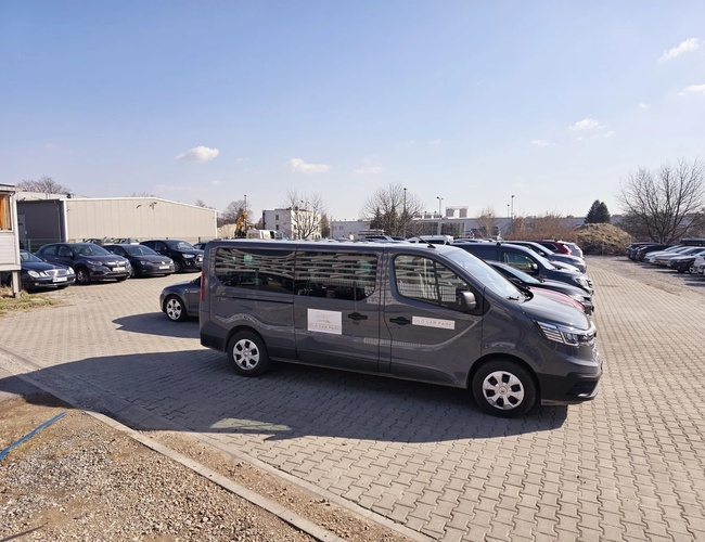 Parkovisko Olo Car Park - Vozidlá stoja na spevnenom námestí. Pozemok je priestranný a čiastočne oplotený. Je slnečný deň.