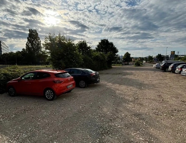 Najvyšší parkovací žehlovač – parkovisko je štrkované a priestranné. Stojí na ňom zaparkované automobily. Územie je obklopené zeleňou.