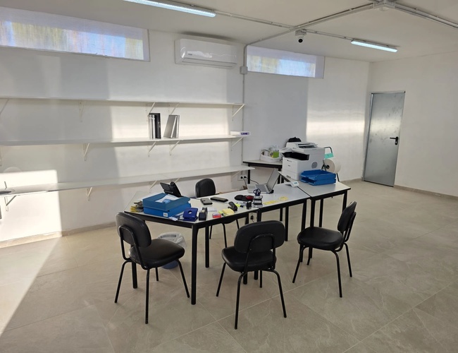 Wnętrze jasnego, przestronnego pomieszczenia biurowego z biurkiem i kilkoma krzesłami.