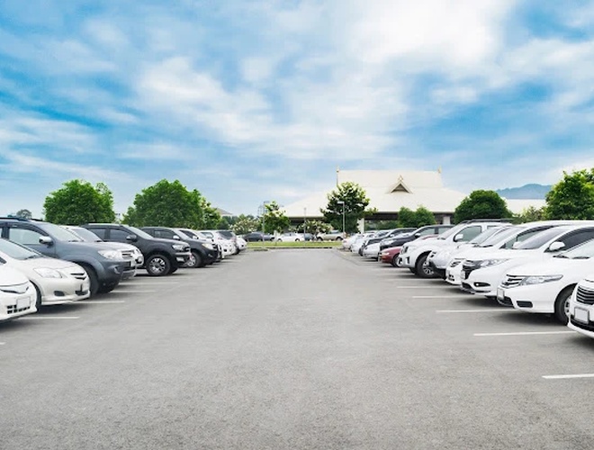 Space Parking Valet – Parkplatz voller Autos auf beiden Seiten. Das Gelände ist offen und von Bäumen umgeben. Der Himmel ist klar und wolkenlos.