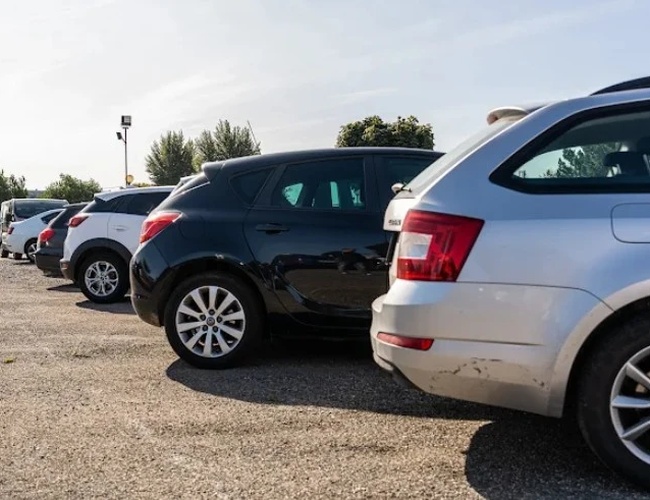 Parking Letim Brno II – kilka samochodów stoi na żwirowanym placu. Teren jest otwarty i nasłoneczniony. W tle rosną drzewa.