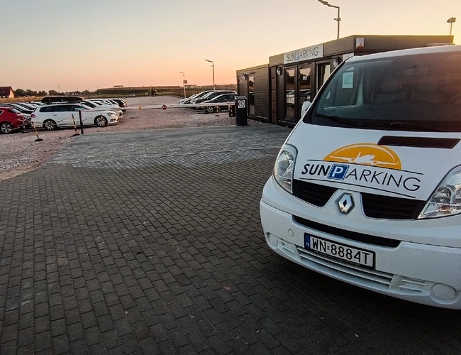 Parkovisko Sun - Biela dodávka stojí na dlažobnej ploche. V pozadí je vidieť zaparkované autá. Areál je otvorený a dobre osvetlený.