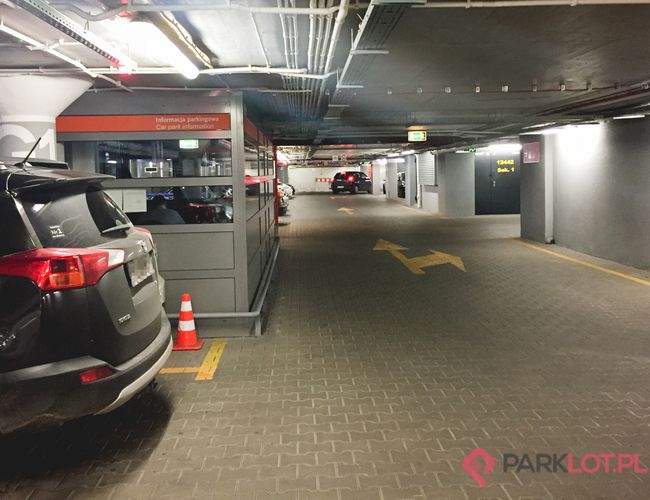 Oficjalny Parking Lotniska P2 - Podziemny parking dla samochodów. Kilka aut zaparkowanych wzdłuż korytarza. Widać oznaczenia kierunkowe na podłodze.