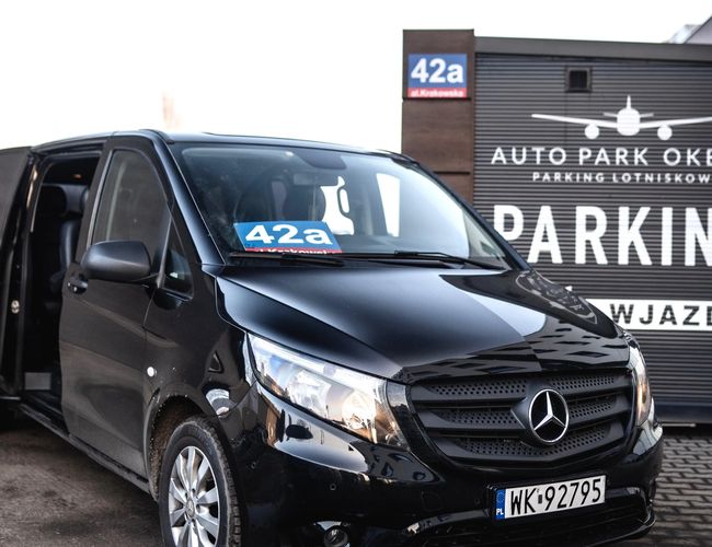 Auto Park Okęcie - Czarne auto z otwartymi drzwiami stoi obok oznakowania parkingu. Tablica rejestracyjna widoczna na aucie.