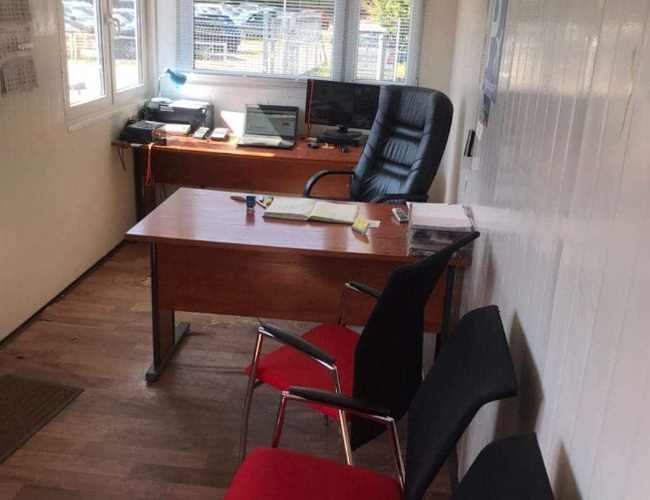 Parkuj Leć – Małe, jasne biuro z dwoma biurkami i krzesłami. Na stole leży laptop i lampka. Za oknem widać samochody.