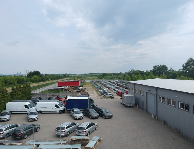 Estacionamiento del Aeropuerto 500 - Estacionamiento para múltiples coches y un edificio. Se puede ver una cerca y árboles verdes de fondo. Los coches están estacionados en un área pavimentada.