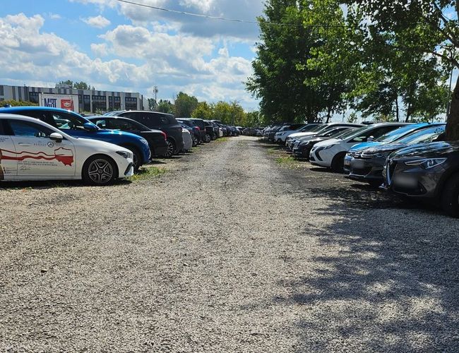 VIP Parking - przy trasie S2. Parking o nawierzchni żwirowej z samochodami. Otoczony drzewami, dobrze oświetlony.