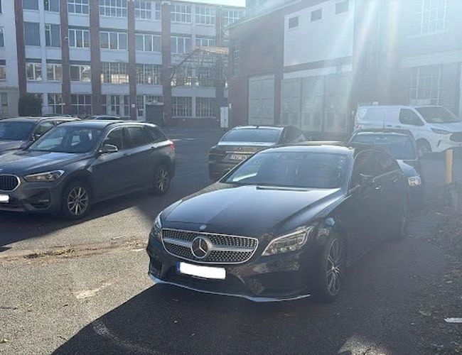 Parking Parkfinder24 Valet – na parkingu stoi kilka samochodów. W tle widać budynek. Teren jest otwarty i słoneczny.
