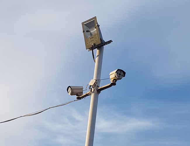 PARKING P24 PREMIUM – Wysoki maszt z kamerami i lampą. Niebo jest jasnoniebieskie z lekkimi chmurami.