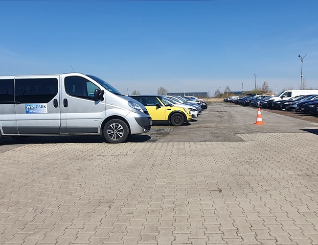 WIZ-PARK – Varios coches están estacionados en una gran plaza abierta. Se puede ver una furgoneta plateada con el logo de la empresa.