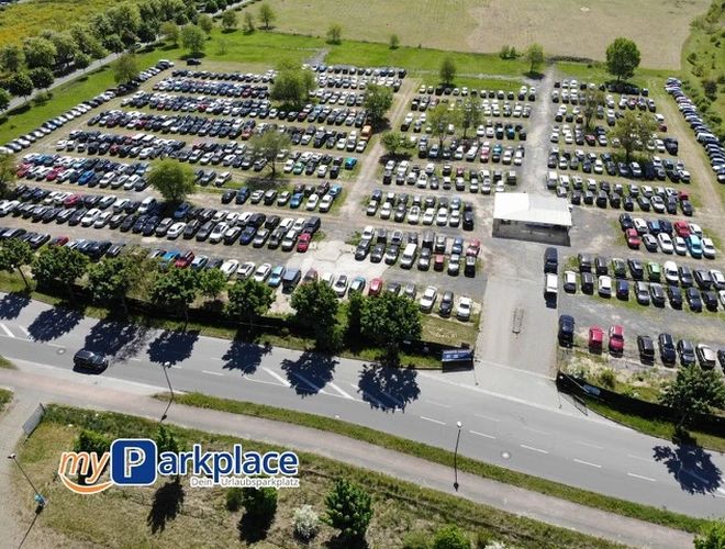 Parking myParkplace - Na parkingu stoją rzędy samochodów. Teren jest otwarty i niezadaszony. Widoczne są drzewa w tle.