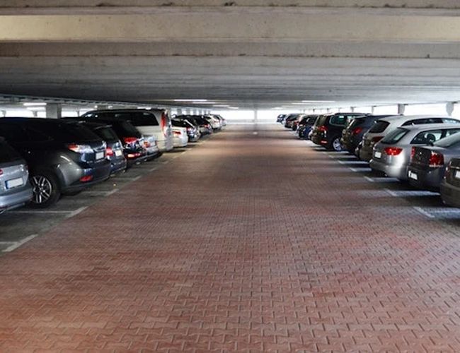 Wnętrze zadaszonego parkingu z miejscami postojowymi po obu stronach. W centralnej części znajduje się droga przejazdowa prowadząca przez parking.