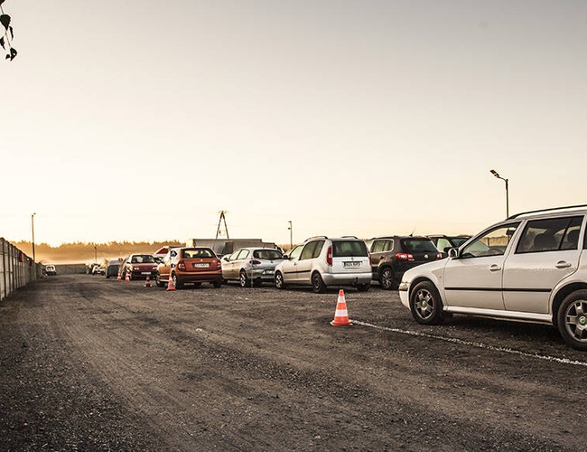 PERI Parking - Estacionamiento con cercado y mantenido en estilo gravilloso. Coches aparcados en paralelo junto a un muro de concreto.