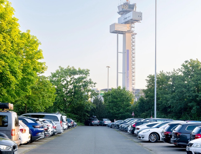 Parking P23 z miejscami postojowymi na świeżym powietrzu oraz wieżą kontroli lotów widoczną w oddali.