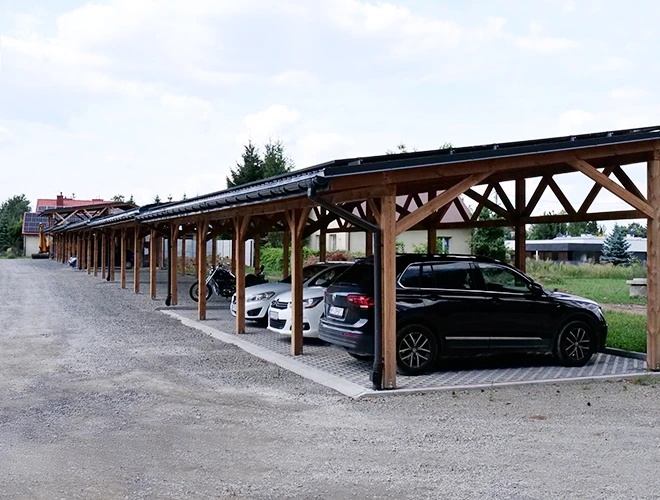 Parking Zielony Kompleks Dwór Ostoya – Estacionamiento cubierto con varios coches. Al lado hay una motocicleta. El terreno es pavimentado y espacioso.