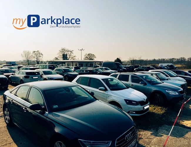 Parkovisko myParkplace – Na parkovisku je veľa áut. Areál je otvorený a ohradený páskou. Na pozadí sú vidieť stromy a budova.