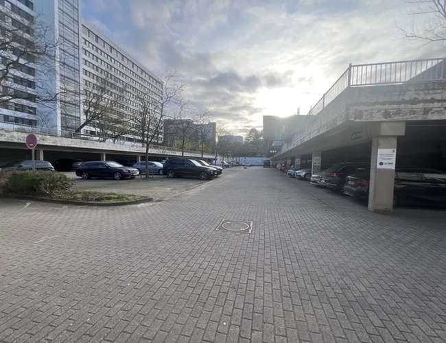 Valet Parking DUS – Utwardzony teren z zaparkowanymi autami. Otwarta przestrzeń między budynkami. Oświetlenie naturalne w pochmurny dzień.